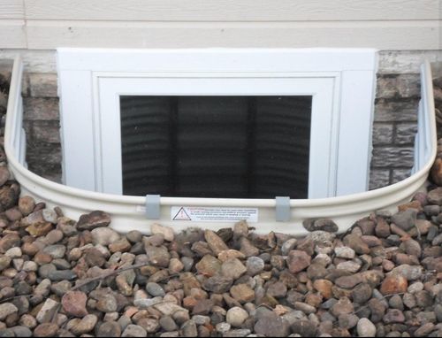 Exterior view of a building with multiple basement window wells along the foundation. Construction site.