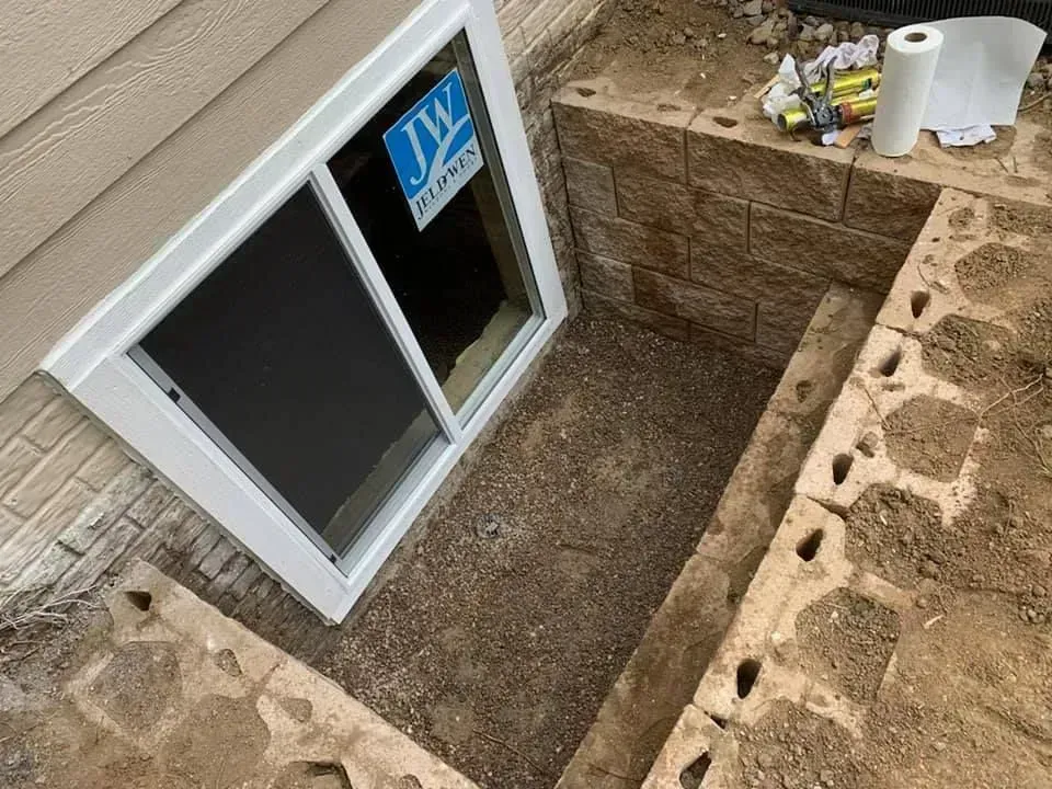 Window well with a new window. Exterior of a house with stacked stone walls and gravel.