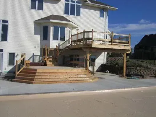 Wooden deck attached to a two-story white house with stairs leading down to a concrete patio.