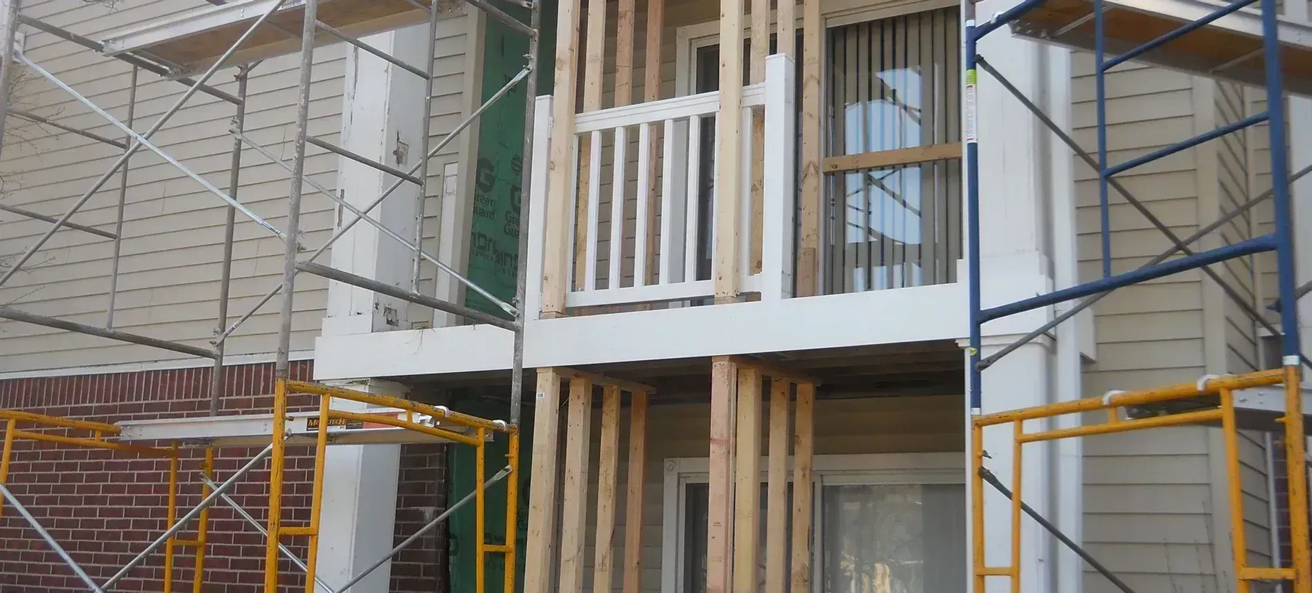 Building exterior with scaffolding and new wooden support beams around a balcony.