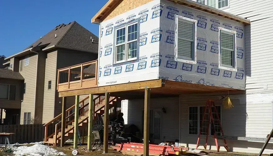 Exterior view of a house addition under construction with a deck, stairs, and wrap.