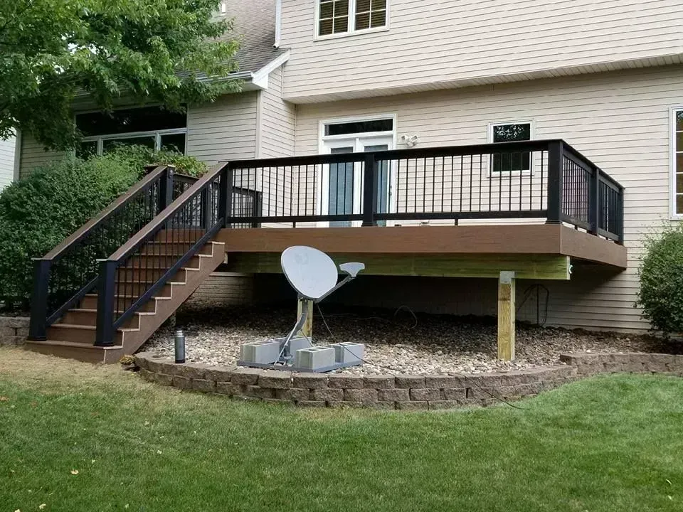 Wooden deck with black railings and steps. Satellite dish beneath. Beige siding background.