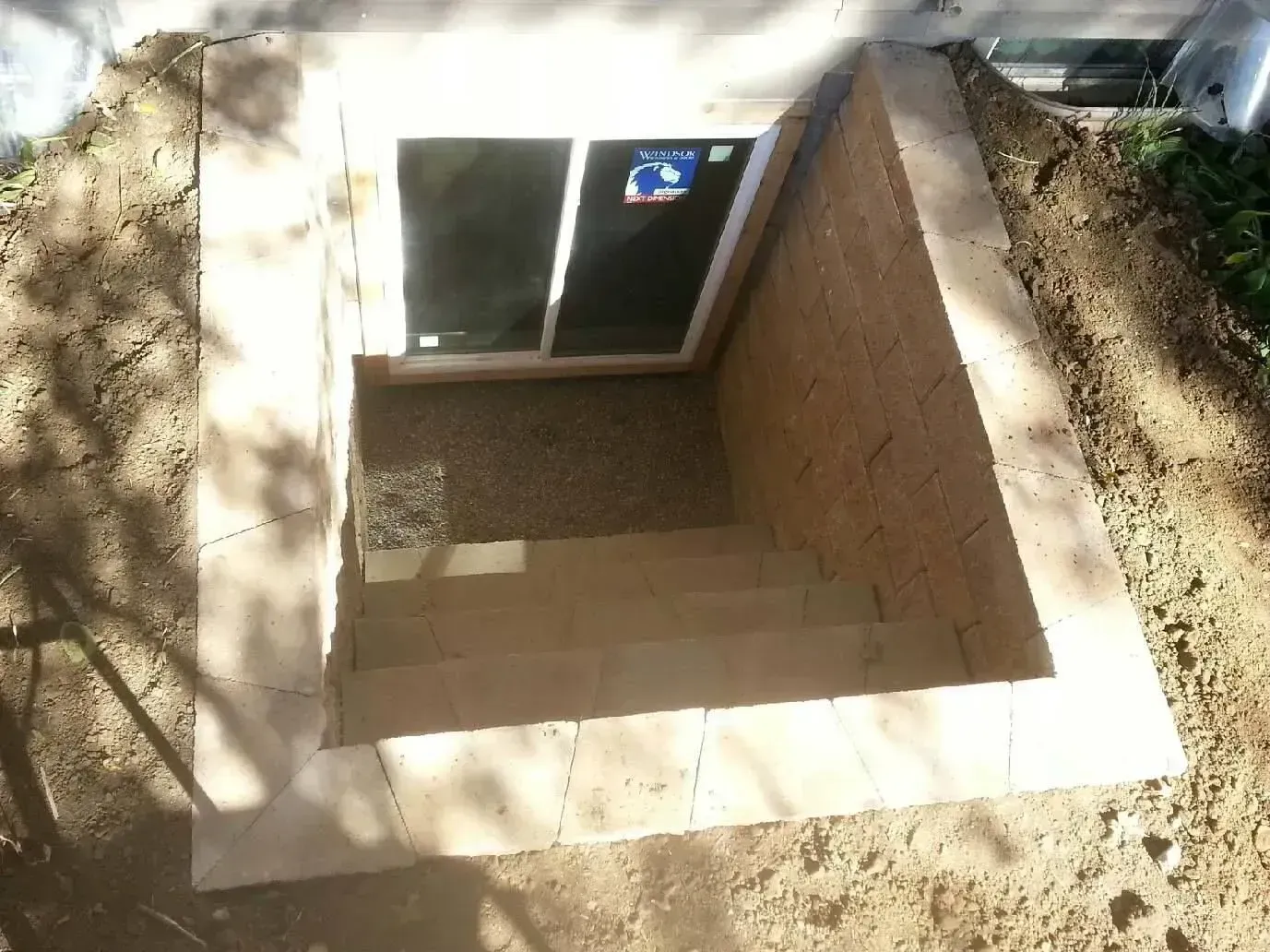 Stone-framed basement entry with steps leading down to a window. Exterior walls are stucco-like, surrounded by dirt.