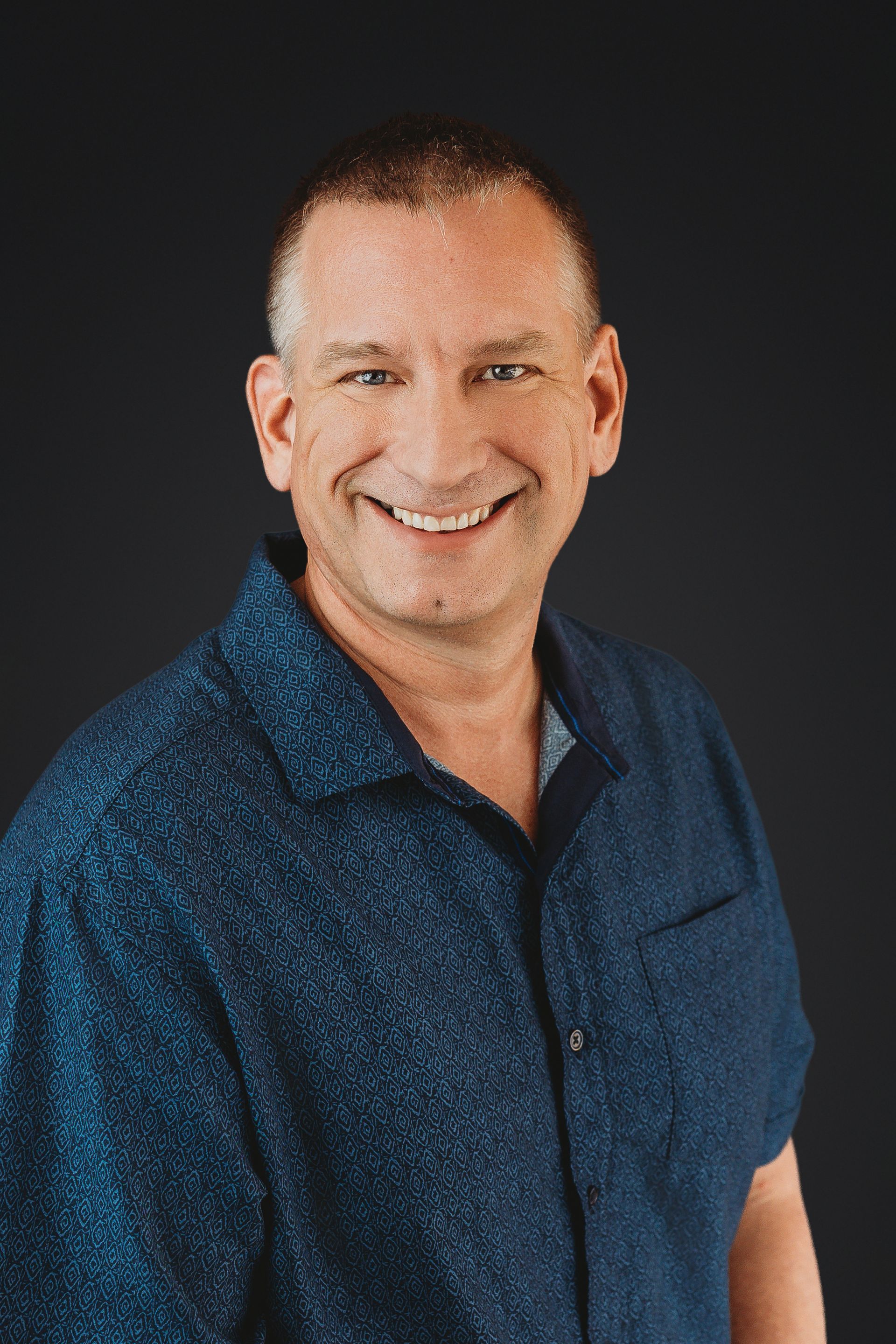 Man in black shirt smiling in front of a white wall.