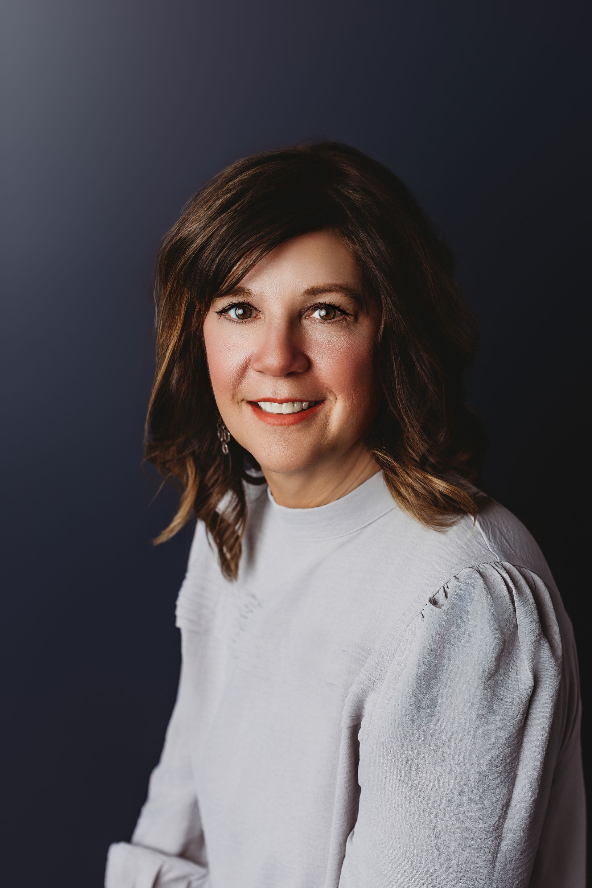 Woman with brown hair, smiling, wearing a black top, against a white background.