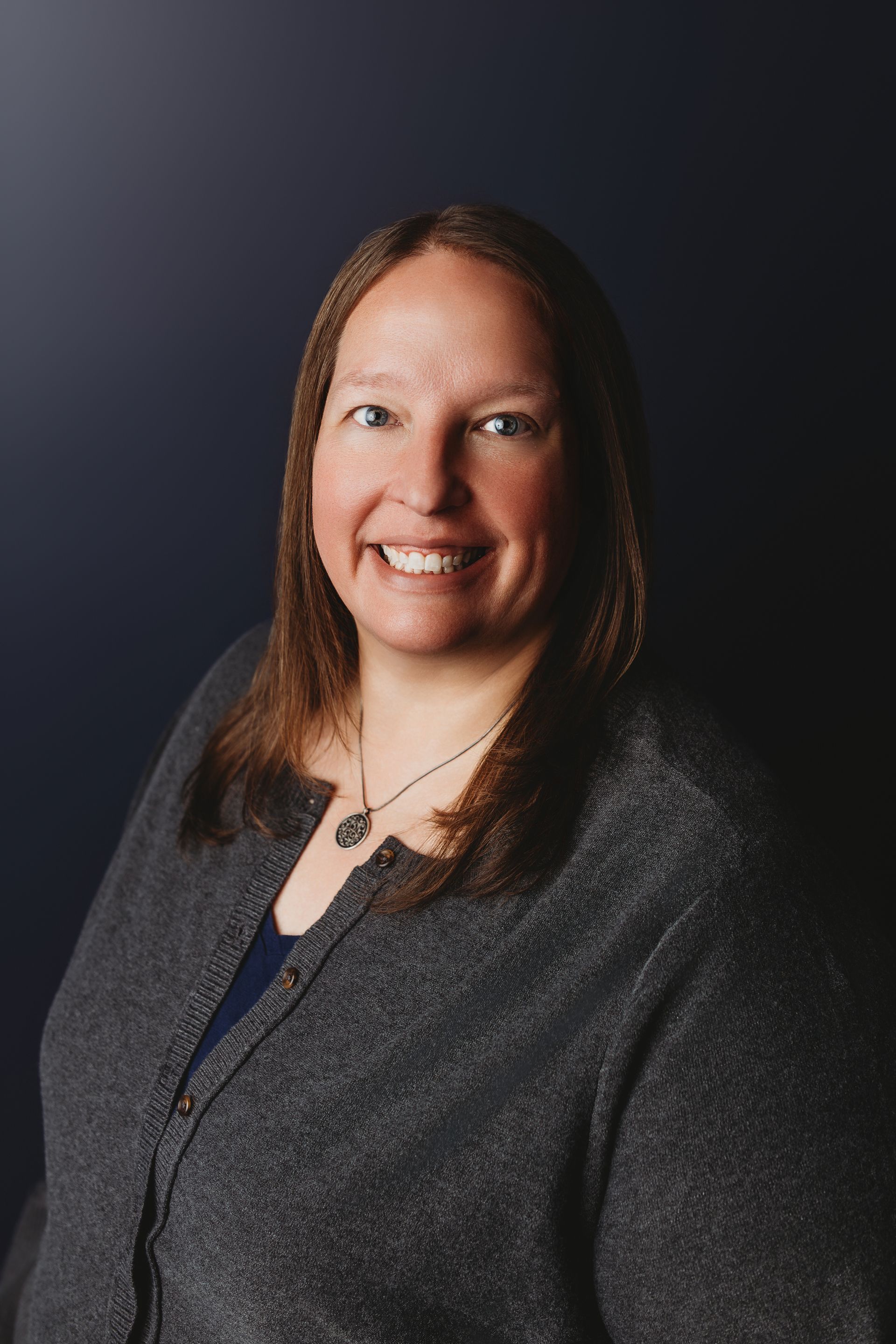 Woman with brown hair, smiling, wearing a black top, against a white background.
