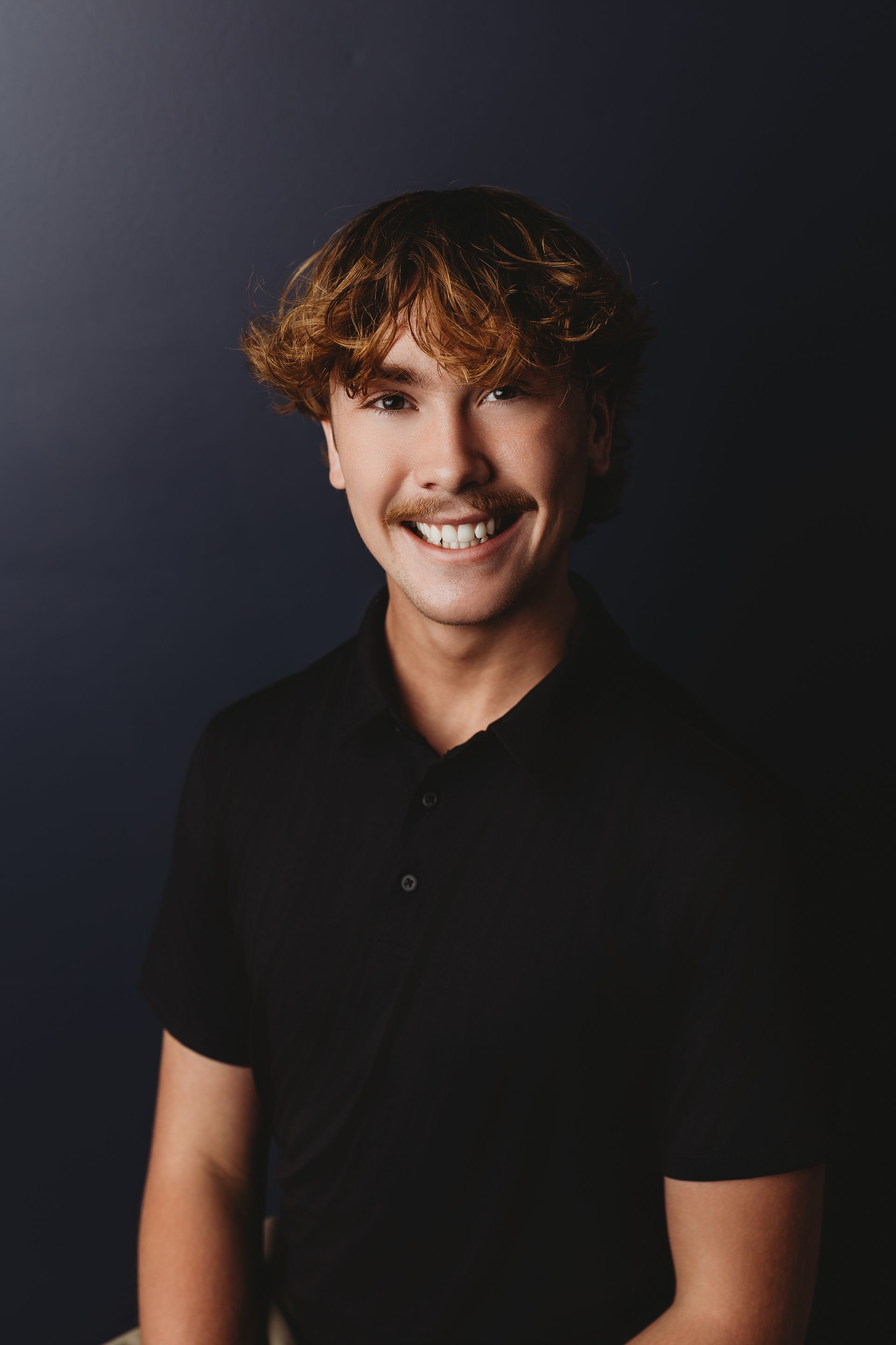 Woman with brown hair, smiling, wearing a black top, against a white background.