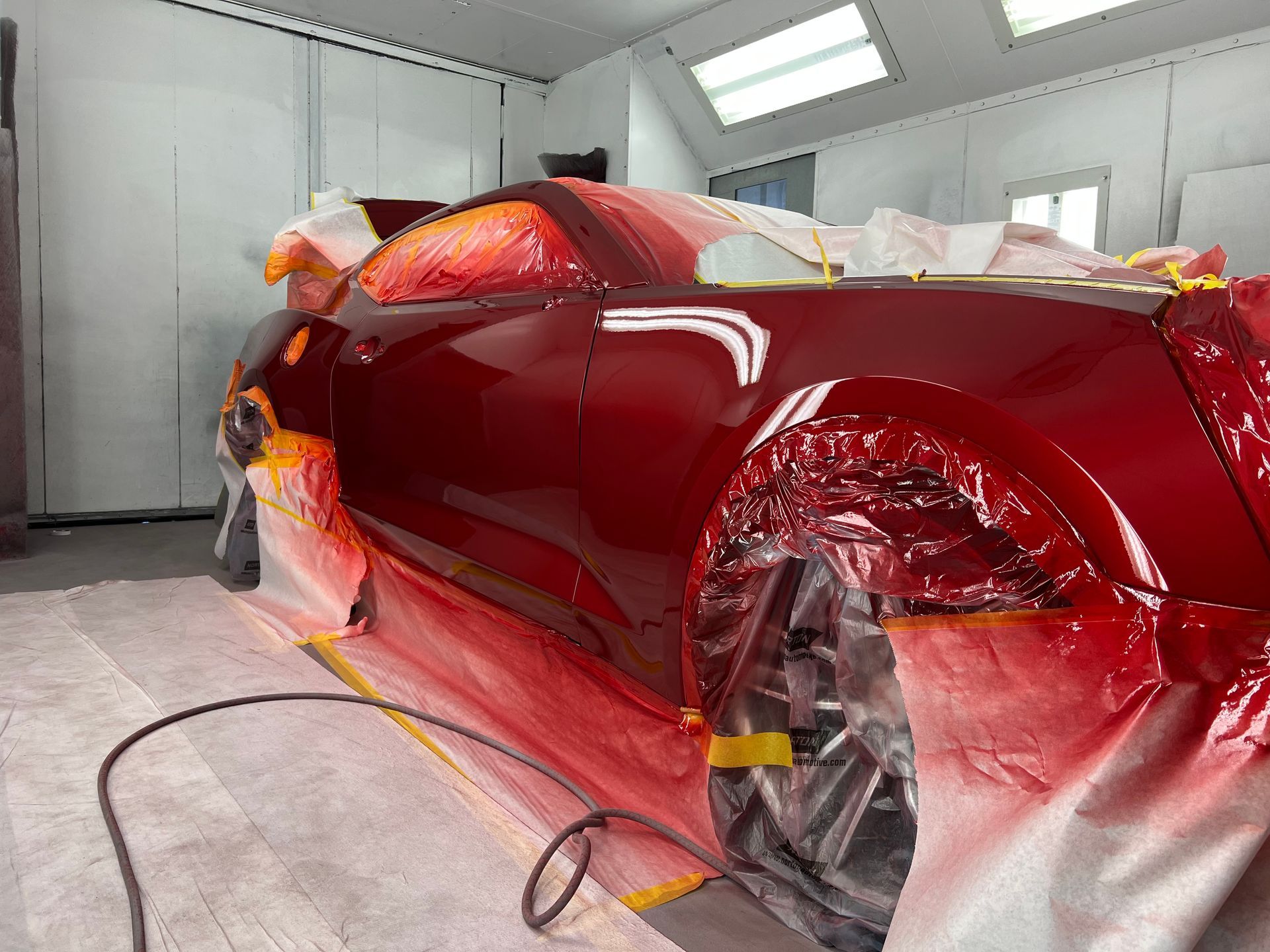 A red car is being painted in a paint booth.
