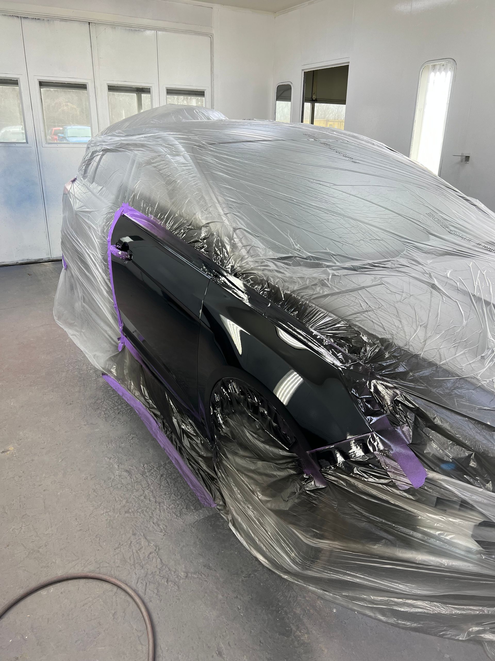 A car is covered in plastic wrap in a garage.