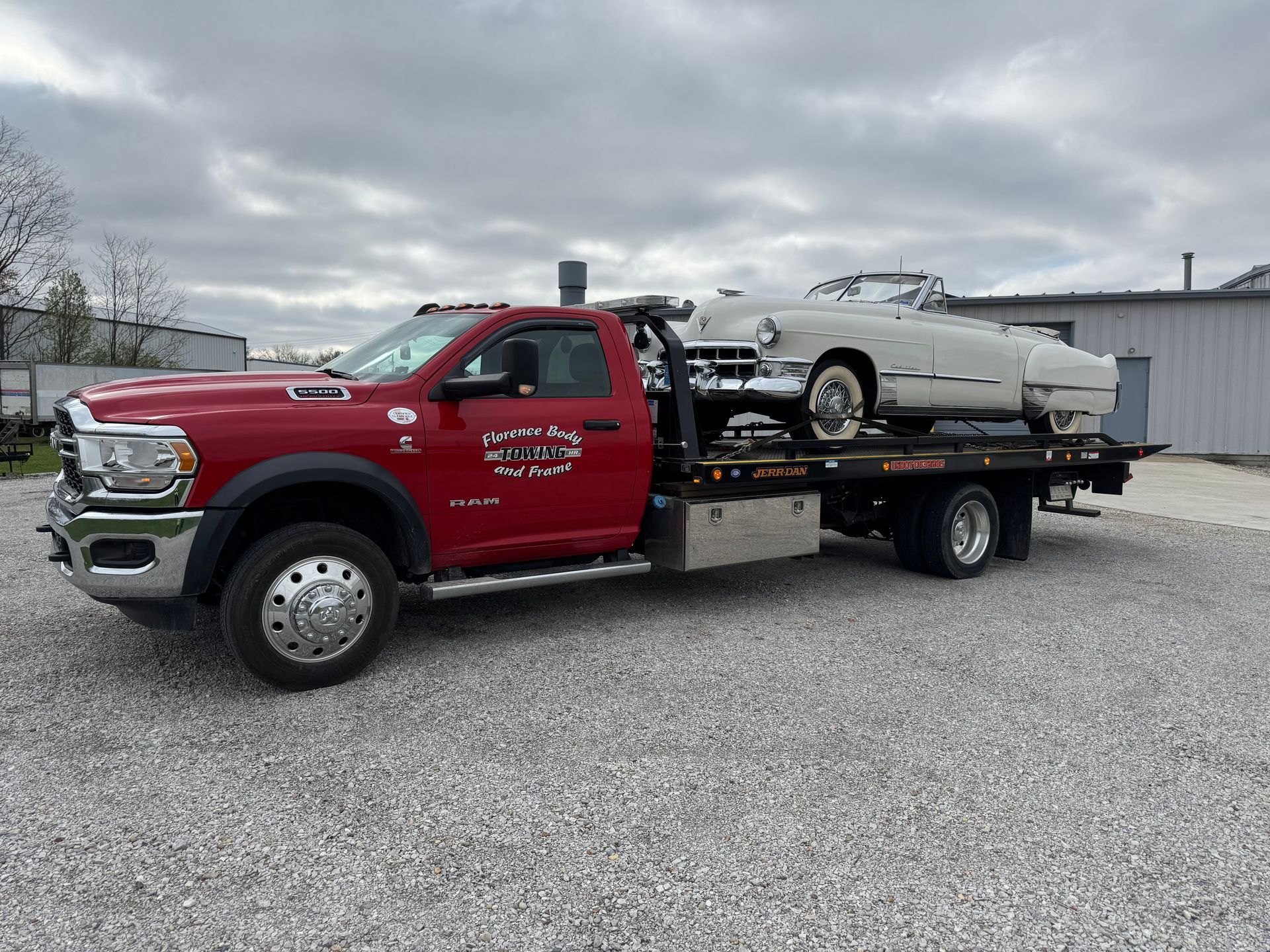 A red tow truck is carrying a white car on a gravel road.