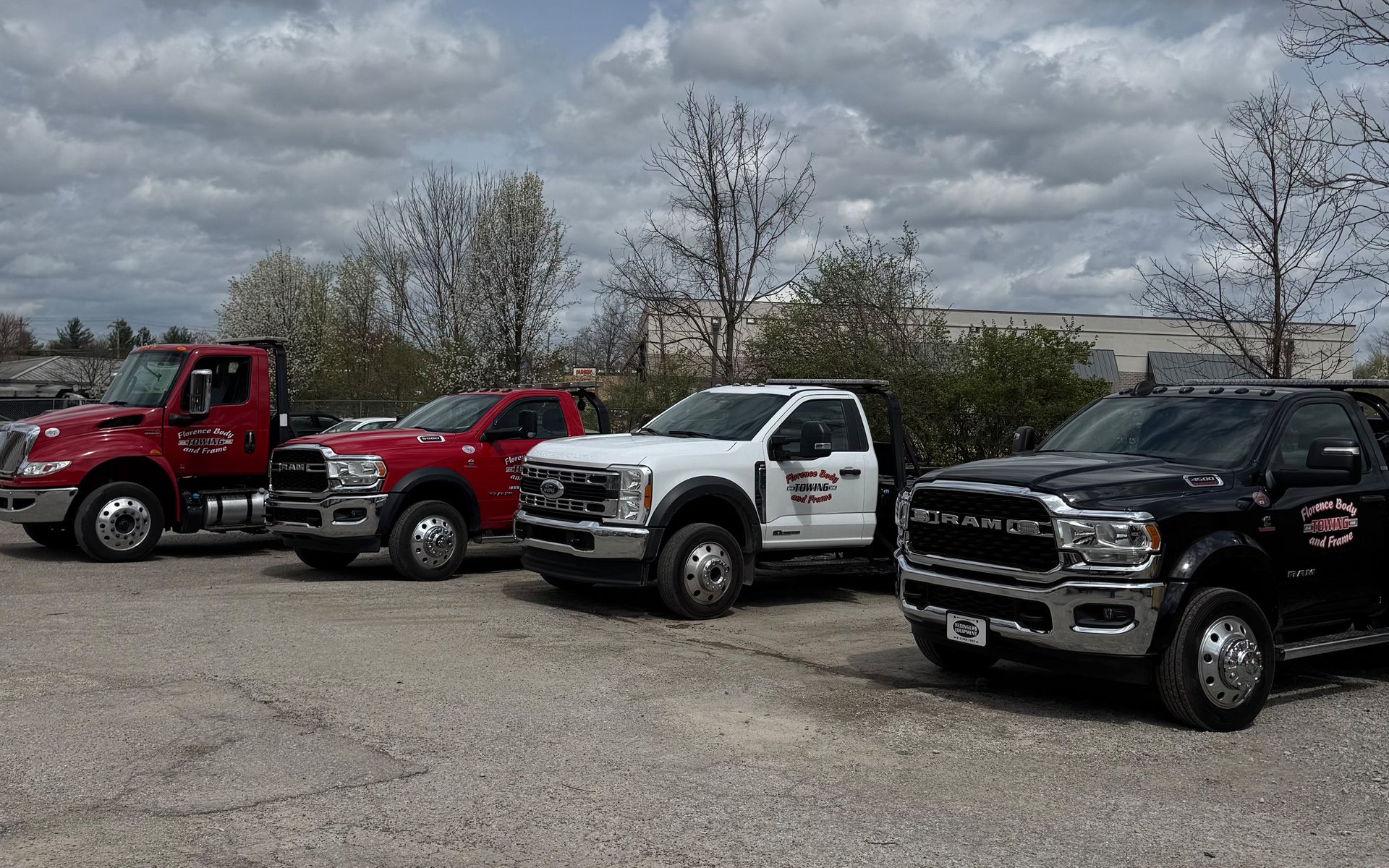 A row of tow trucks are parked in a parking lot.