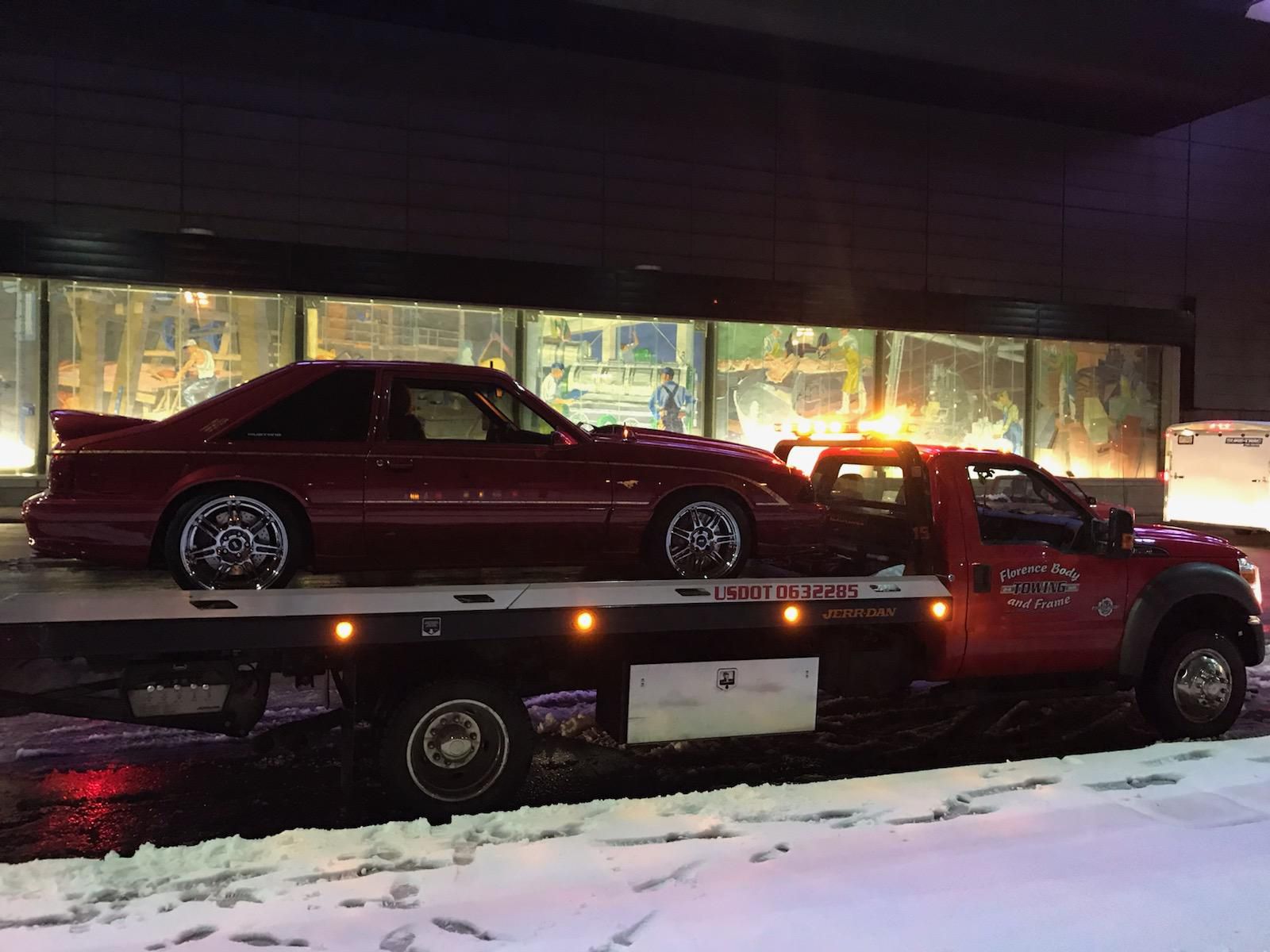 A red car is being towed by a tow truck