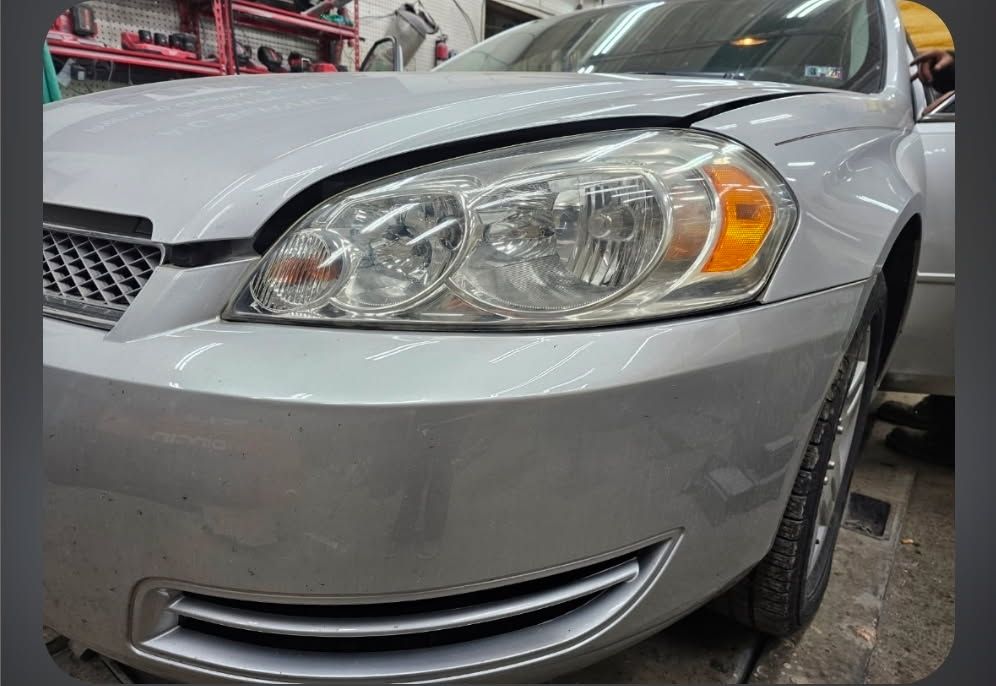 A glossy black 1967 Chevrolet Camaro parked on a gravel driveway in front of a white building and bare trees.