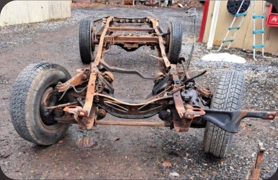 A classic muscle car in primer grey sits partially restored in an auto body workshop.