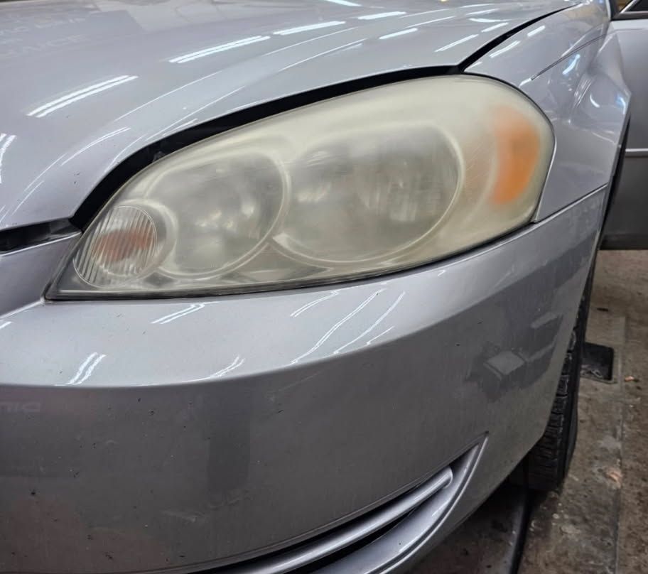 A classic muscle car in primer grey sits partially restored in an auto body workshop.