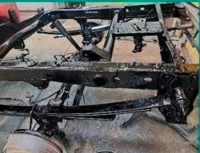 A glossy black 1967 Chevrolet Camaro parked on a gravel driveway in front of a white building and bare trees.