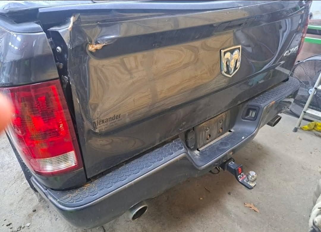 Damaged black Dodge Ram truck tailgate with dent; broken taillight and bumper.