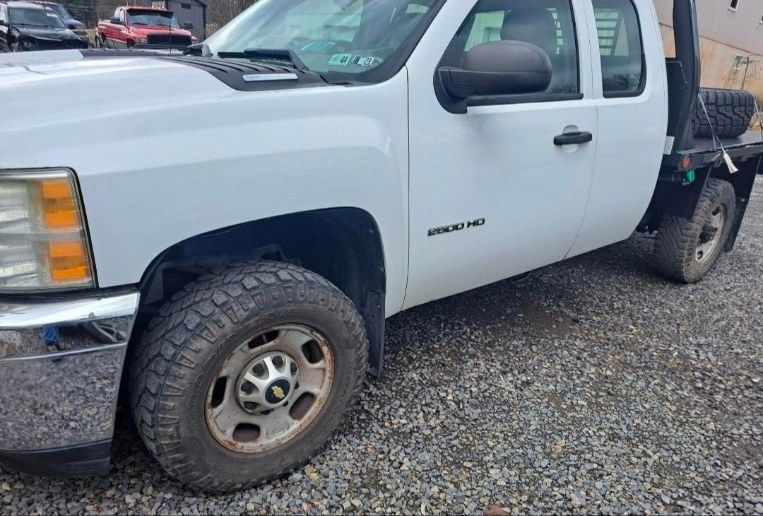 White Chevrolet Silverado 3500 HD truck with a flatbed in a gravel lot.