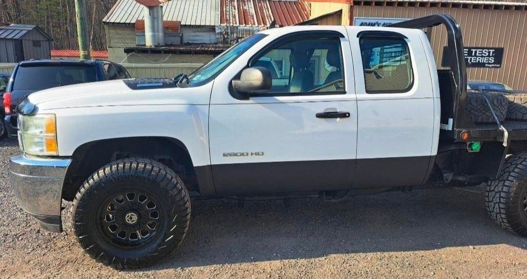 White and black pickup truck with a flatbed in front of a building.