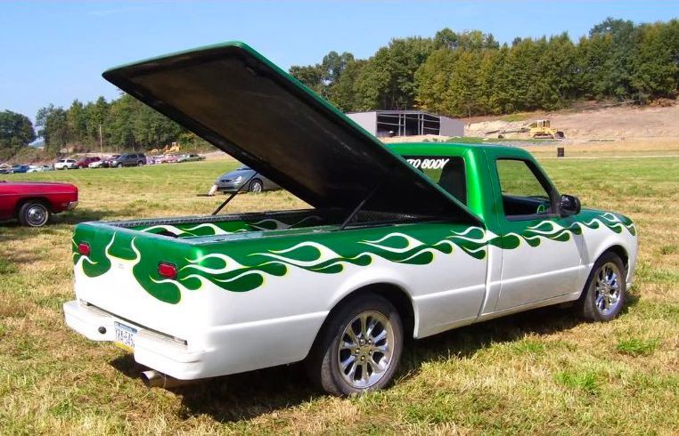 White and green custom pickup truck with flames, tonneau cover open, parked on grass.