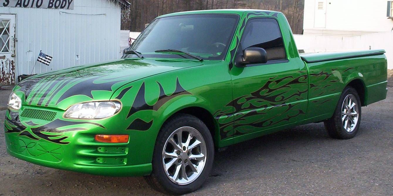 Green pickup truck with tribal decals, chrome wheels, parked in front of a building with a 'body shop' sign.