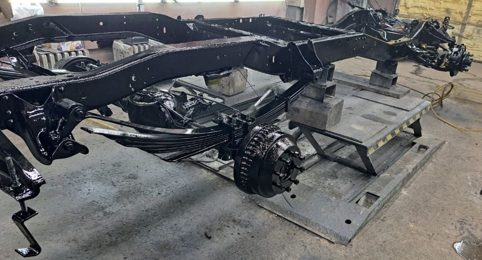 Black painted truck chassis on a metal stand, in a workshop.
