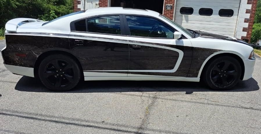 A white Dodge Charger with a custom black and dark marbled graphic side wrap and black wheels parked outdoors.