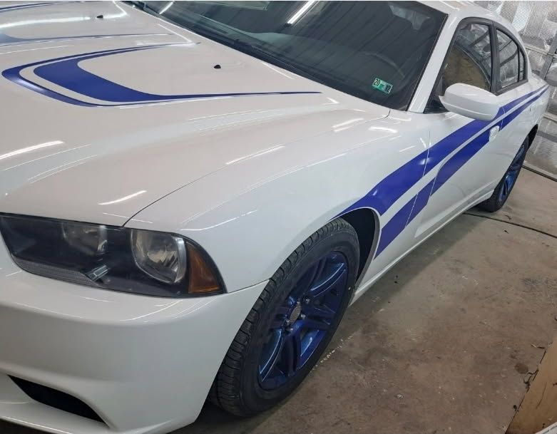 A white Dodge Charger with blue racing stripes and matching blue rims parked indoors on a concrete floor.
