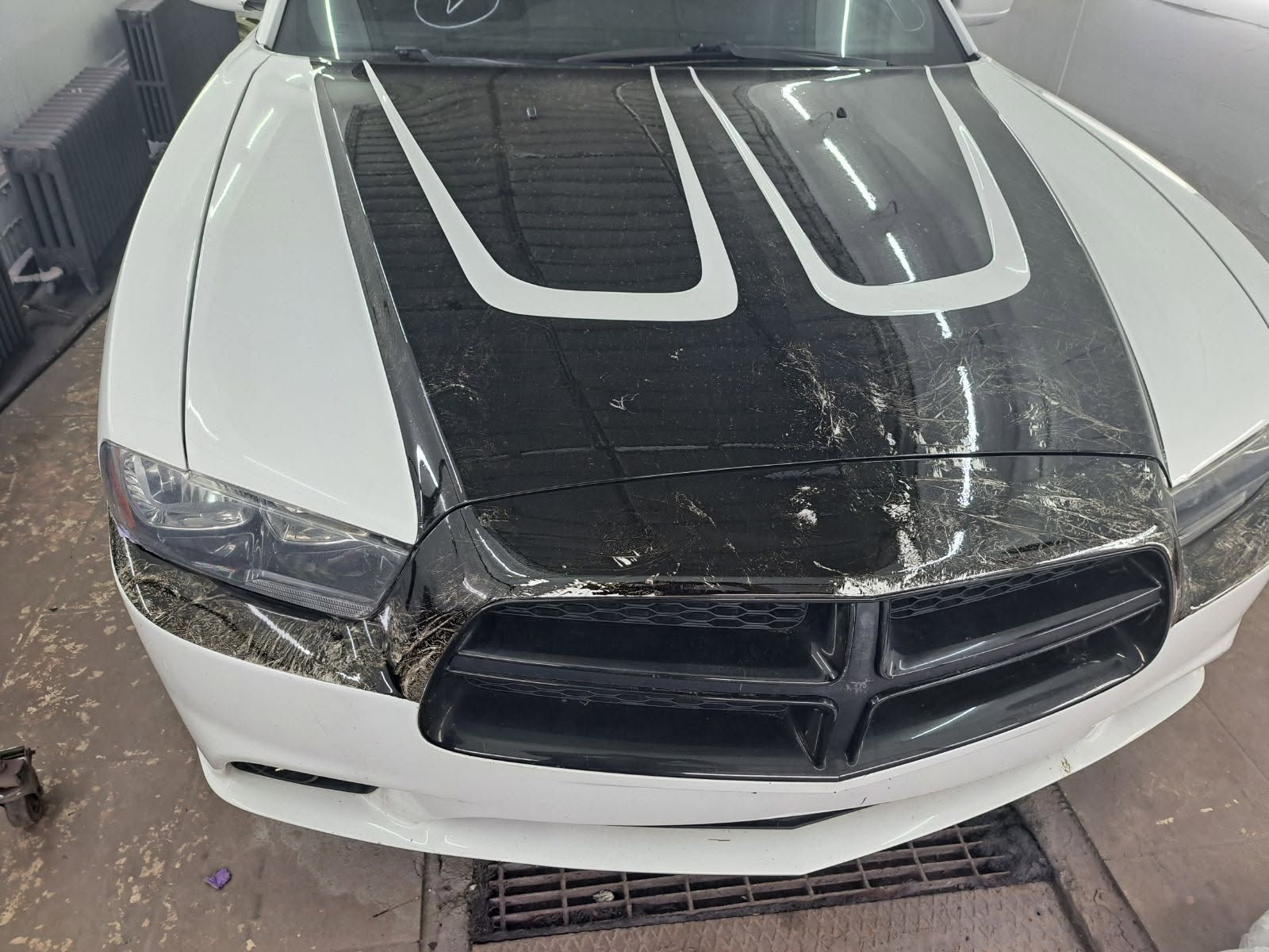 A white Dodge Charger with a black hood featuring dual white racing stripes in an auto shop.