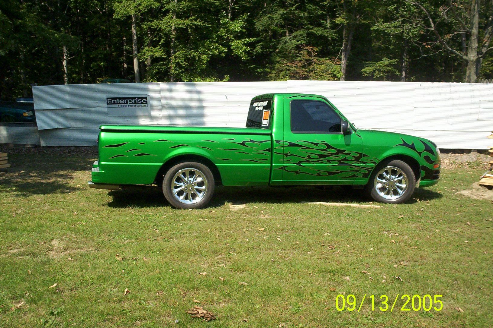A lime green custom pickup truck with black flame decals, parked on grass with a fence in the background.