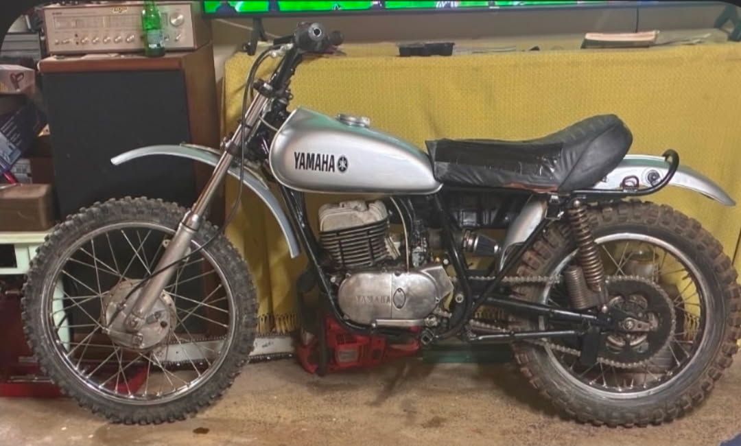 A vintage silver Yamaha dirt bike parked indoors against a yellow backdrop.