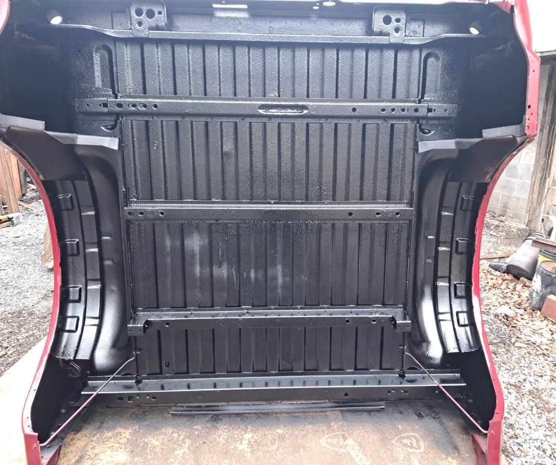 An interior view of a red truck bed liner with black vertical ridges and reinforcement bars, set outdoors.
