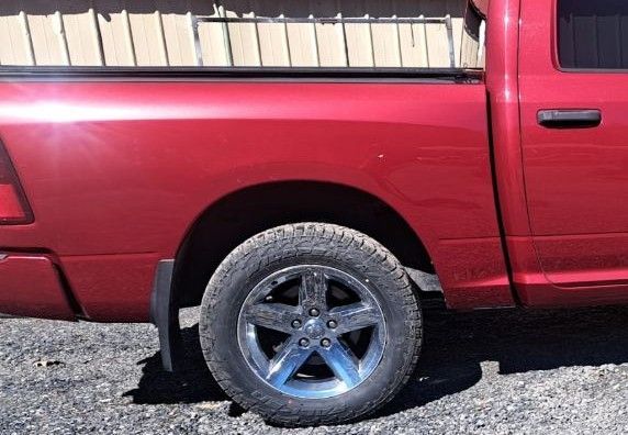 A close-up side view of a red pickup truck bed and its rear wheel, parked on a gravel surface.