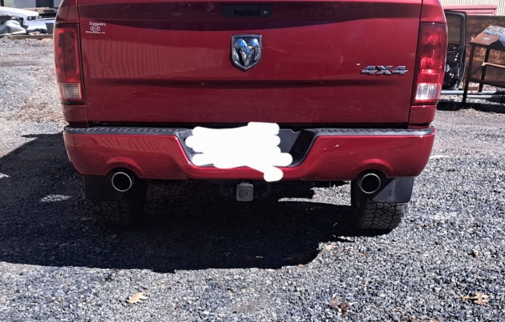 A red Ram 4x4 pickup truck viewed from the rear, showing dual exhaust pipes, a trailer hitch, and a blurred license plate.
