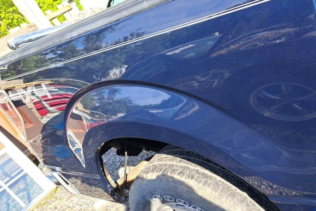 Blue car with damaged rear wheel arch and dented body panel, viewed close-up.