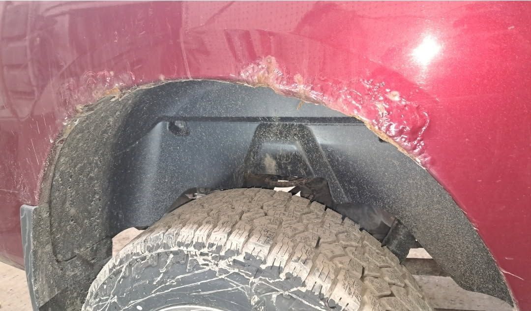 Close-up of a red car’s wheel arch with a black mud flap and a dirty tire.