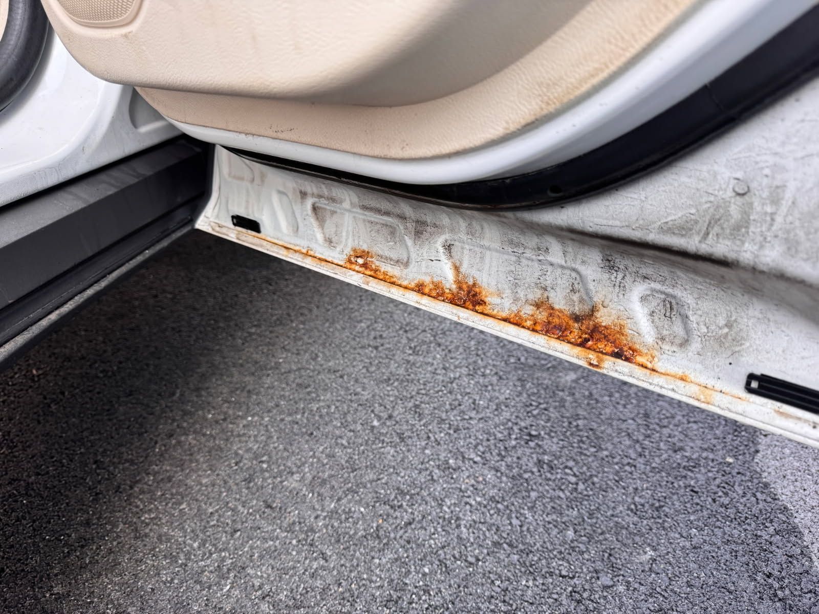 Rusty metal car door sill with beige seat and dark carpet floor mat
