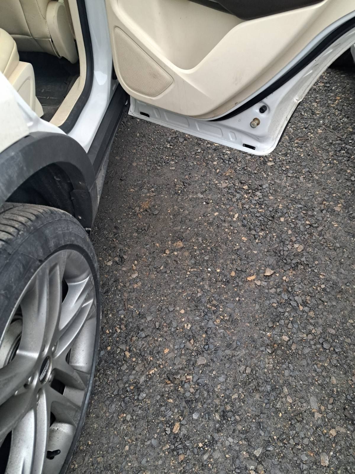 Open the car door beside a wheel on rough pavement.
