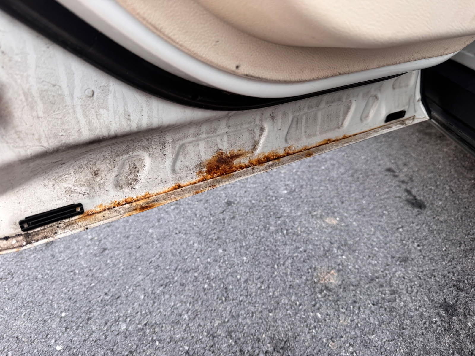 Rusty metal seam along a car door sill above gray carpeted flooring.