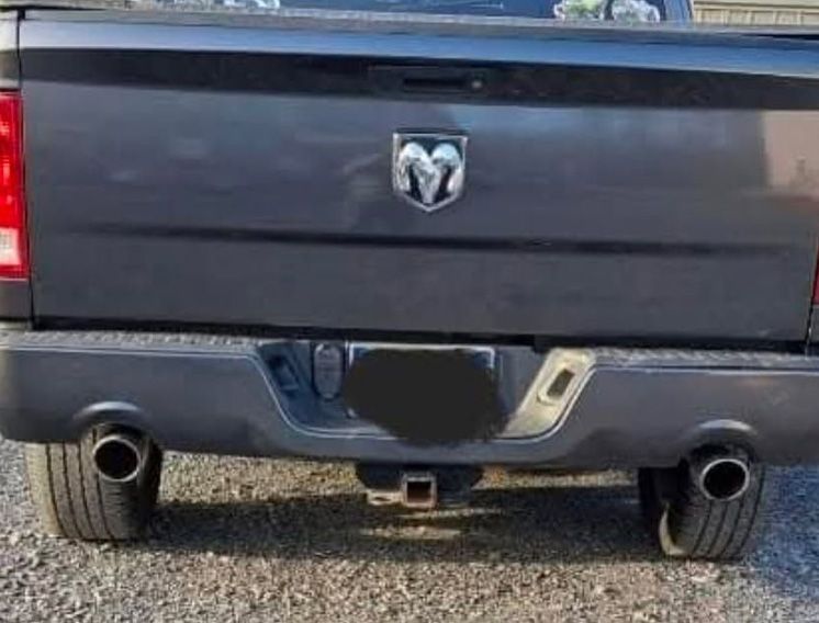 Black Dodge Ram truck's rear end with Ram emblem, black bumper, dual exhaust, and trailer hitch.