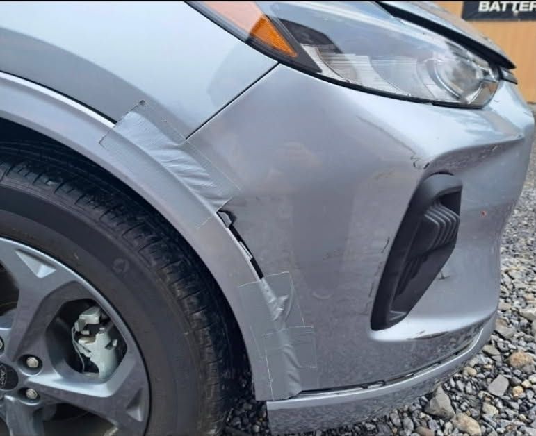 Close-up of a gray car’s front-left side with scratches and dent damage near the wheel arch.