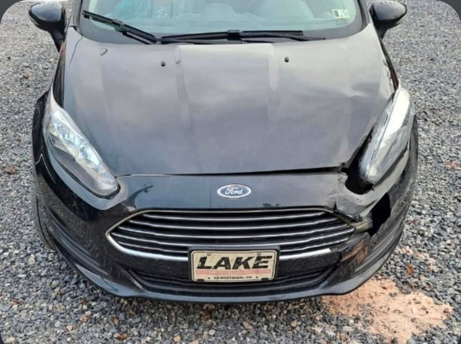 Front view of a black Ford car with a Lake license plate on a gravel surface.