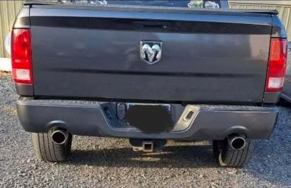 Rear view of a dark gray Dodge pickup truck with dual exhausts and a trailer hitch, parked on gravel.