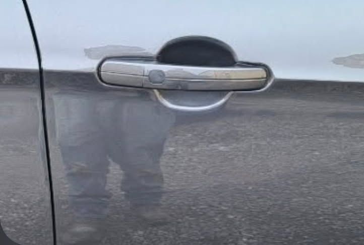 Close-up of a gray car door handle with a visible vertical scrape and scuff marks below it