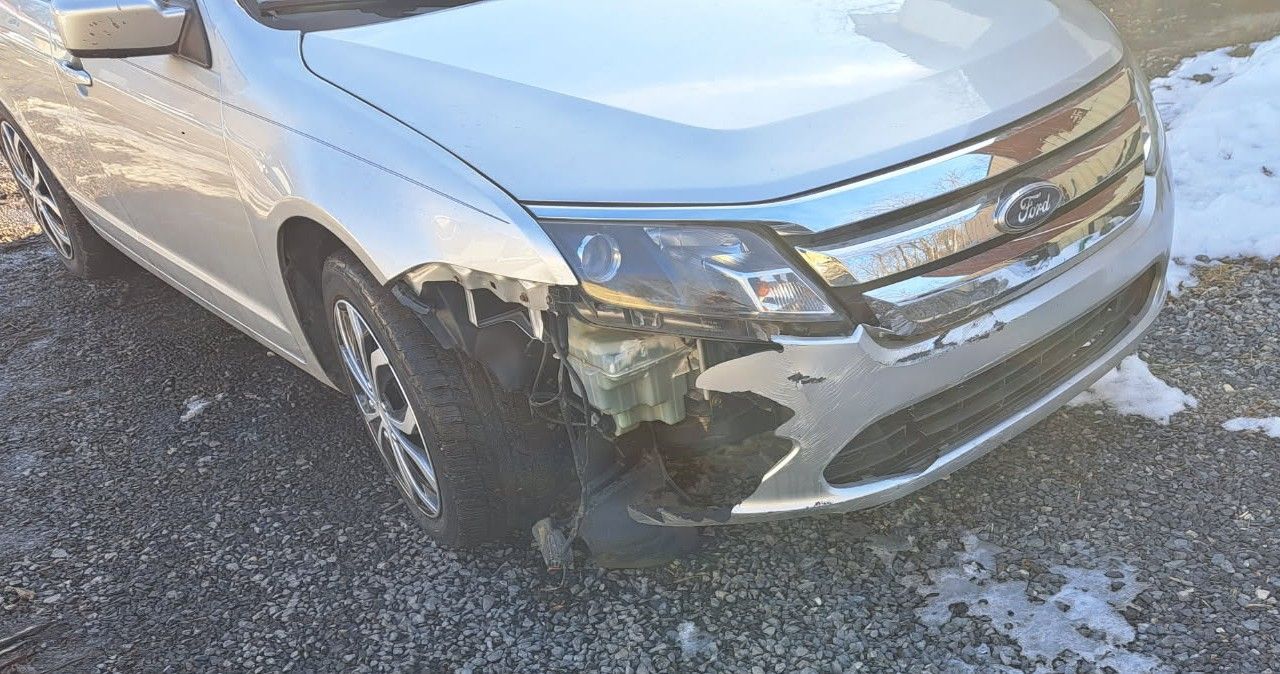 Silver sedan with front-left bumper damage and a flat tire on a snowy road.