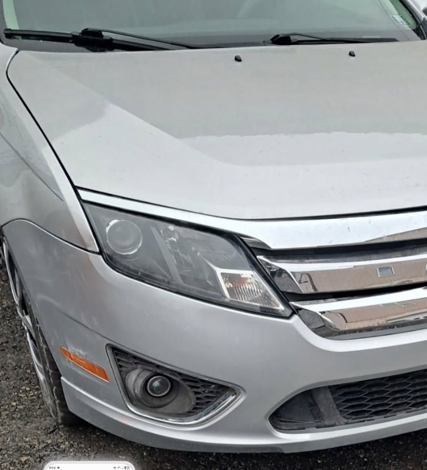Close-up of a silver car’s front end and headlights in a parking lot