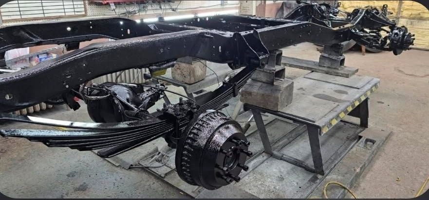 A glossy black 1967 Chevrolet Camaro parked on a gravel driveway in front of a white building and bare trees.