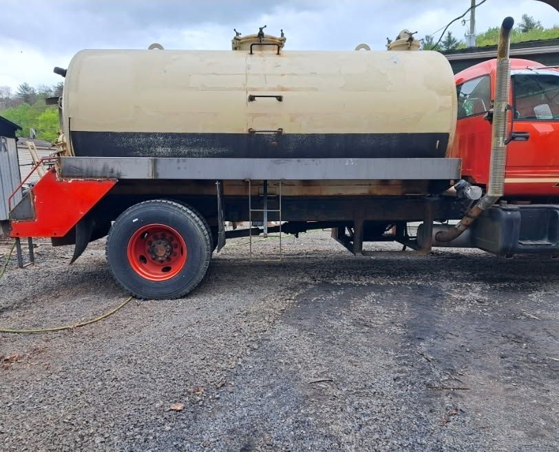 Cream-and-red tanker truck parked on gravel under a cloudy sky.
