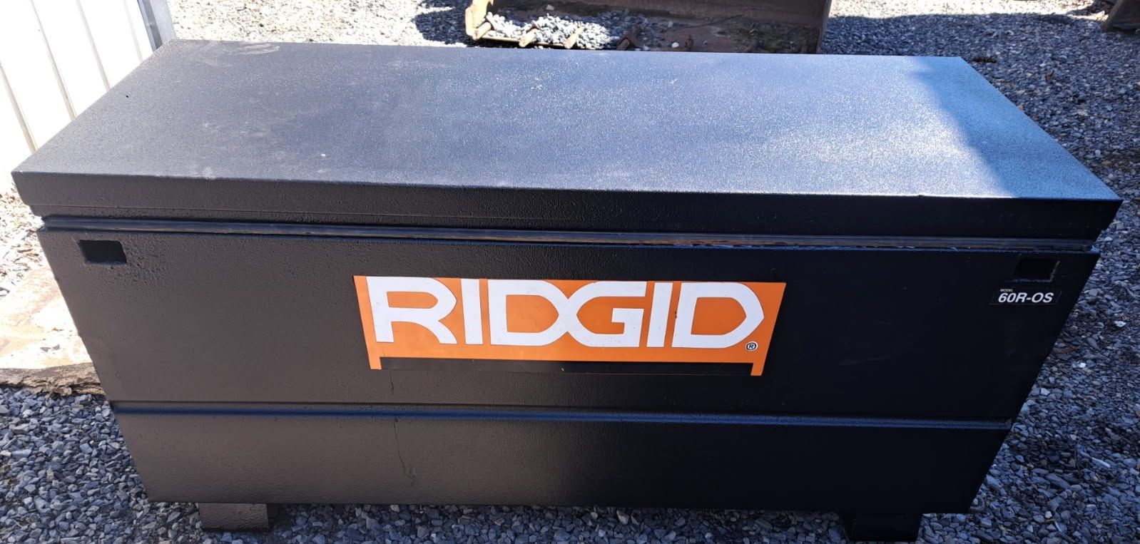 Black RIDGID toolbox with orange logo, sitting outdoors on gravel.