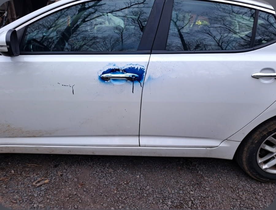 Side view of a silver car with a blue scratch and dent on the rear door handle area
